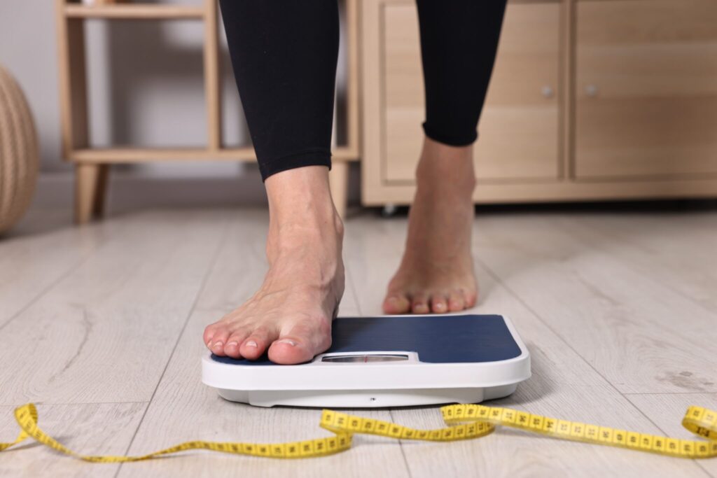 Woman,Stepping,On,Floor,Scale,And,Measuring,Tape,At,Home,