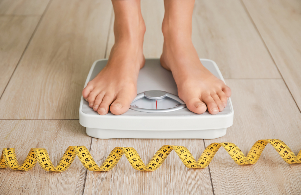 A close-up shot of a woman standing on a scale with a tape measure in front of her