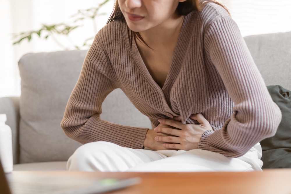 A cropped shot of a woman bent over, holding her stomach because of symptoms of food intolerances